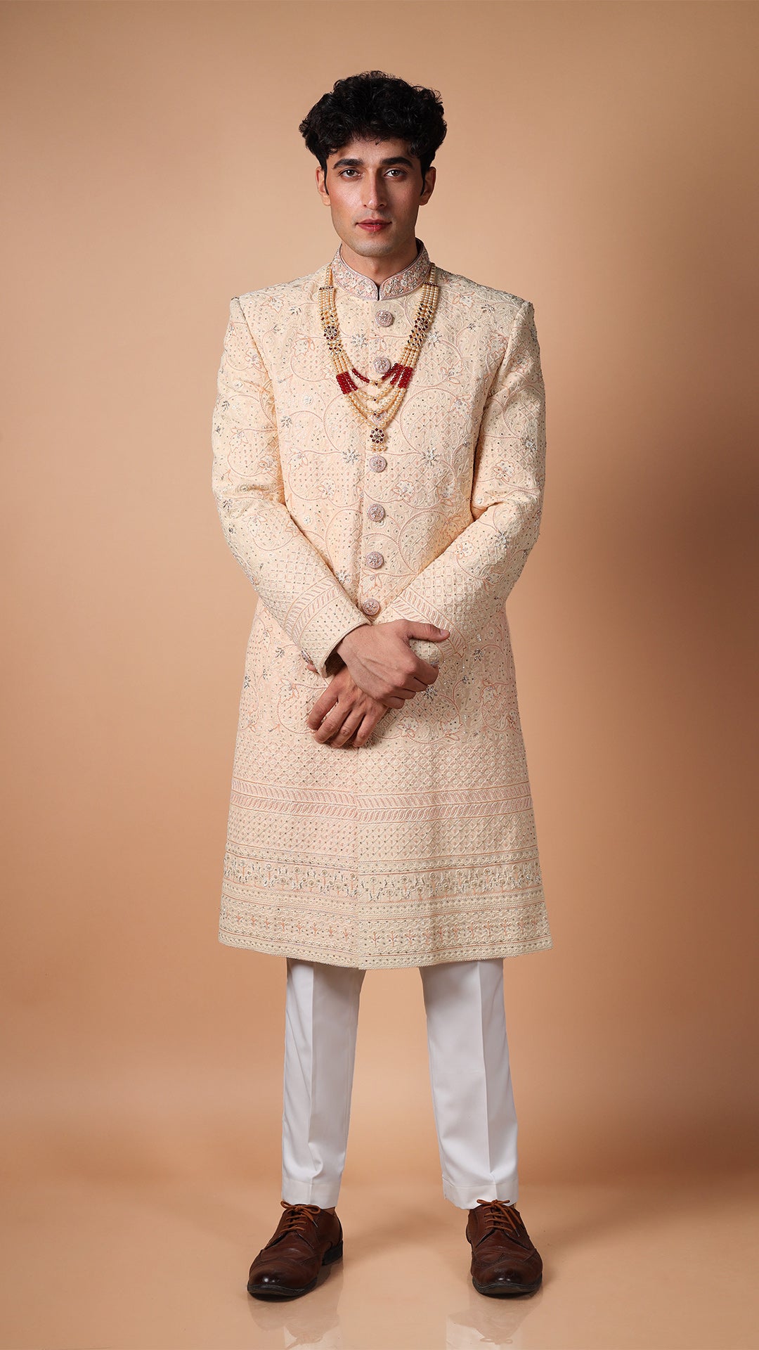 The model strikes a dynamic pose, bringing movement to the Peach Lucknowi Hand Embroidered Sherwani. The traditional craftsmanship and sophisticated charm of the ensemble make it perfect for weddings and grand celebrations.